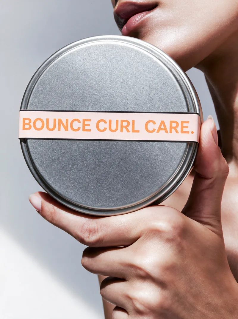 A hand holding the Bounce tin lid, reading Bounce Curl Care